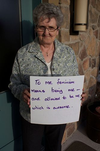 Woman holding sign reading: 'To me feminism means being me - and allowed to be me which is awesome'