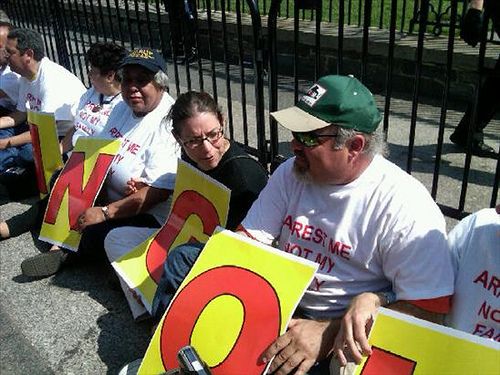 Protesters sit in front of the White House wearing shirts that Arrest Me Not My Family and holding signs