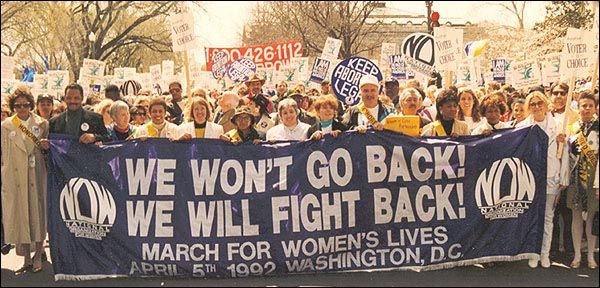 photo from march, group of people holding large purple banner with the words We won't go back We will fight back