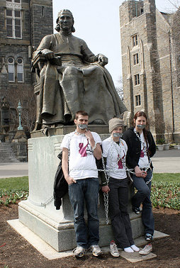 three students chained to a statue, with tape over their mouths