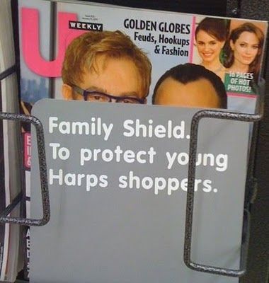 Cover of US weekly with Elton John and husband, mostly blocked by a gray plastic cover that says Family Shield. To Protect Young Harps Shoppers