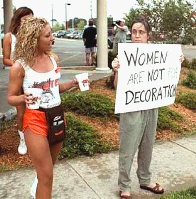 A woman holds a sign reading, 'A woman is not for decoration' next to a Hooter's employee in uniform.
