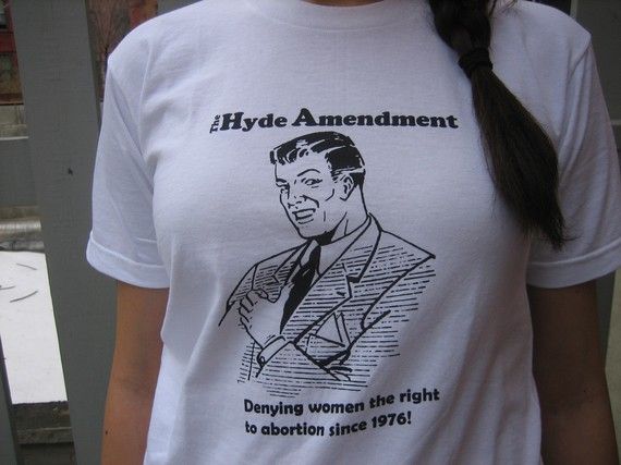 White t-shirt with graphic of guy that says Hyde Amendment/Denying women the right to abortion since 1976