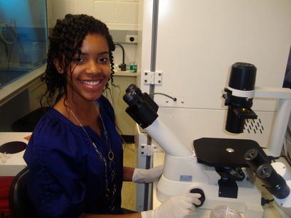A smiling Katie Washington sits in front of a microscope