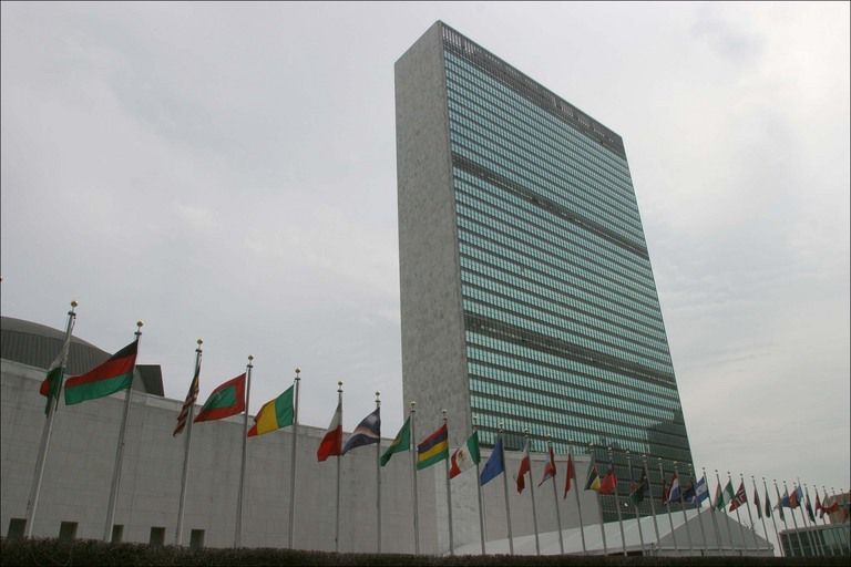 the iconic united nations building with the flags of numerous countries waving outside in the breeze